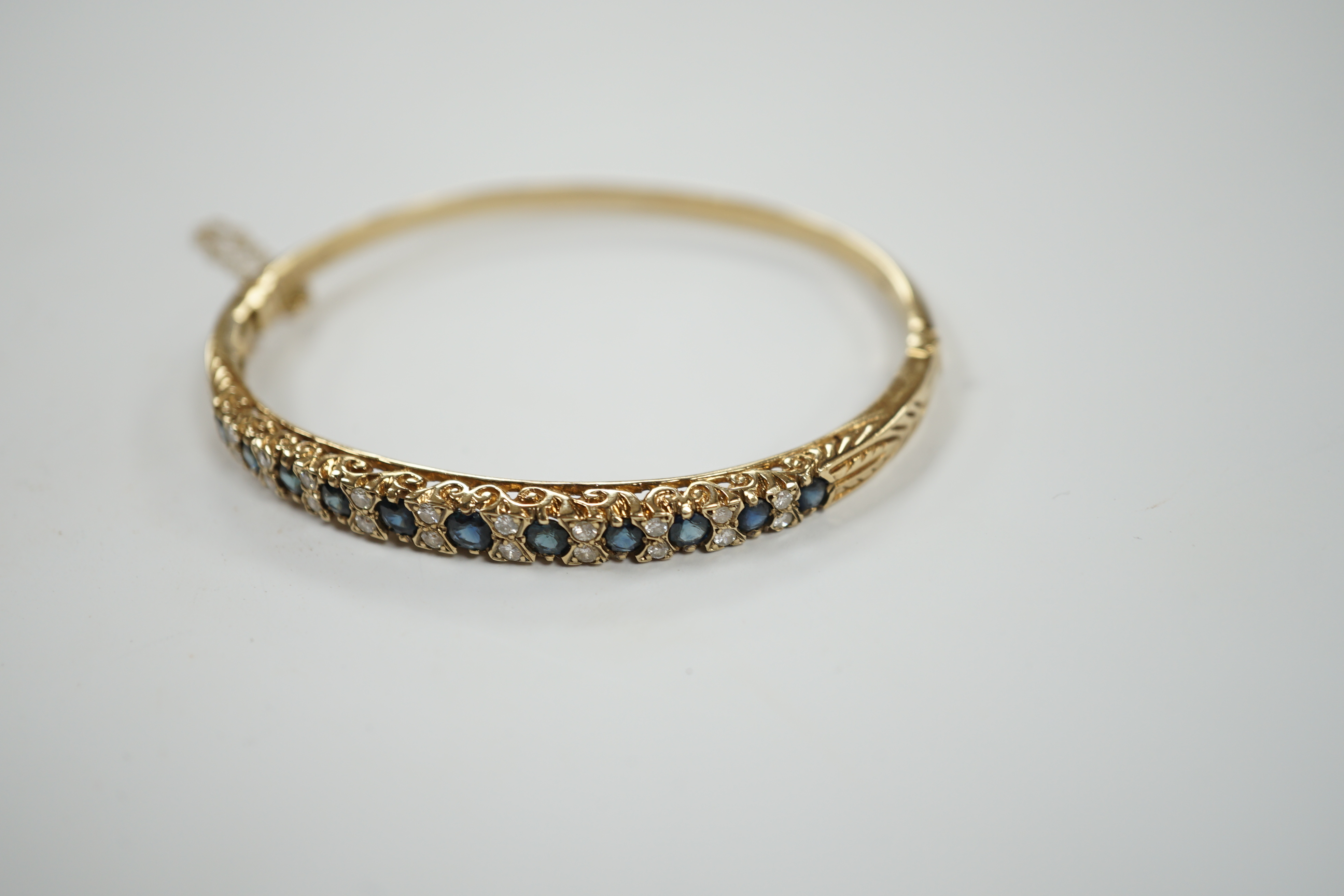 A modern 9ct gold, sapphire and diamond cluster set hinged bangle, gross weight 14 grams.